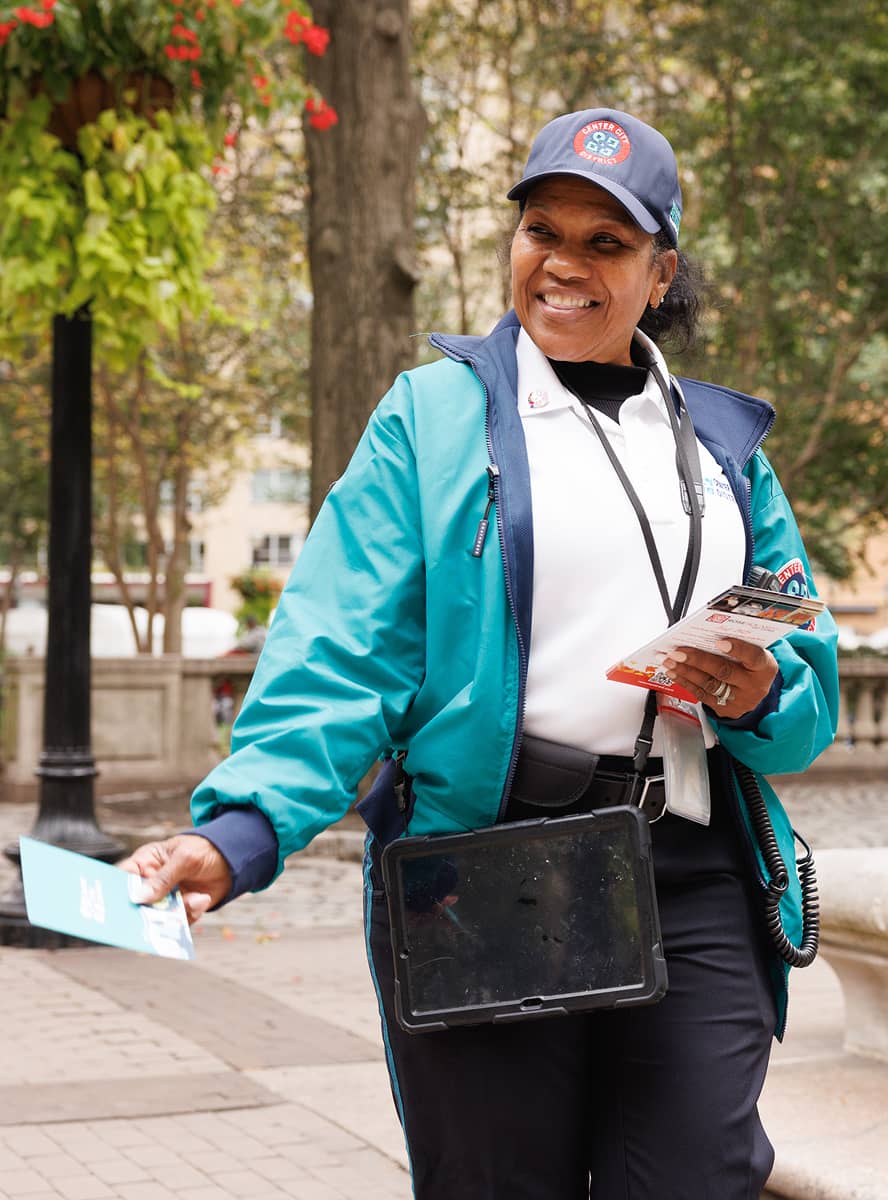 A CCD community service representative (CSR for short) safety ambassador wearing a uniform and carrying a 2-way radio, handing out brochures.